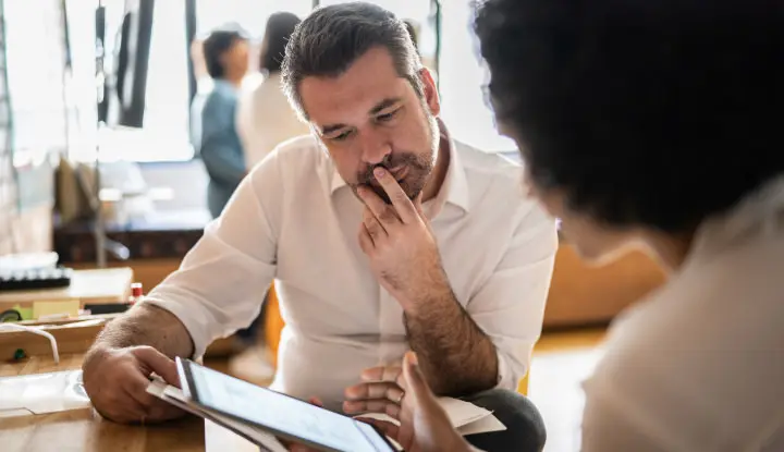 2 people thoughfully look over options displayed on a tablet device.