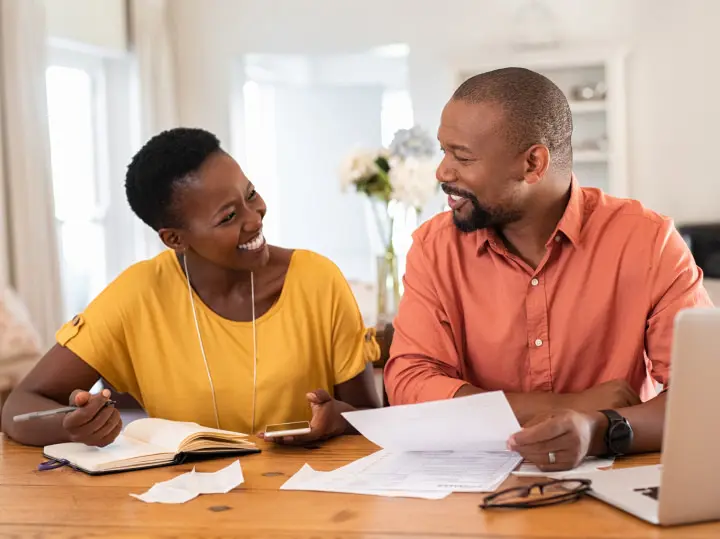 A couple sit together happily organizing their finances and paperwork.